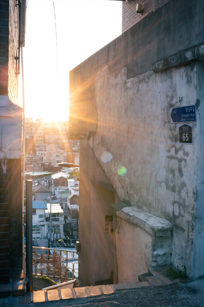 Golden hour sunlight shining through a narrow stairway between buildings in Changsin 6-gil