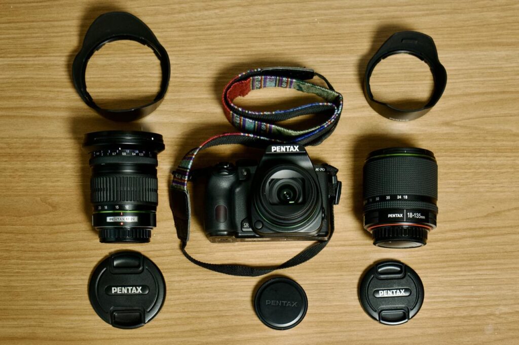Flat lay of a Pentax K-70 camera with three lenses arranged on a wooden surface, prepared for winter photography.