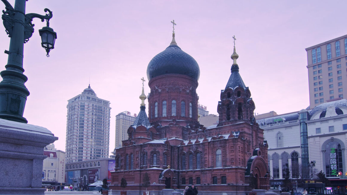 Saint Sophia Cathedral in Harbin photographed in winter under hazy morning light, with surrounding city buildings in the background.