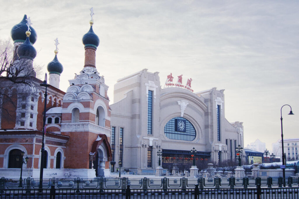 Harbin Railway Station photographed in winter, with Saint Iver Church, a Russian Orthodox church, visible beside the station building.