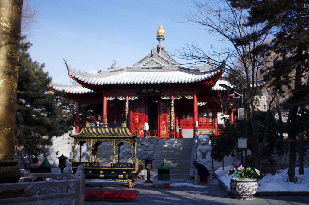 A red wooden hall at Jile Si in Harbin, photographed in winter with snow on the ground and visitors walking through the courtyard.