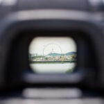 View through a Nikon D610 viewfinder fitted with an Eg-Af split-prism focusing screen, showing Namsan Seoul Tower centered behind the autofocus and spot-metering mark.