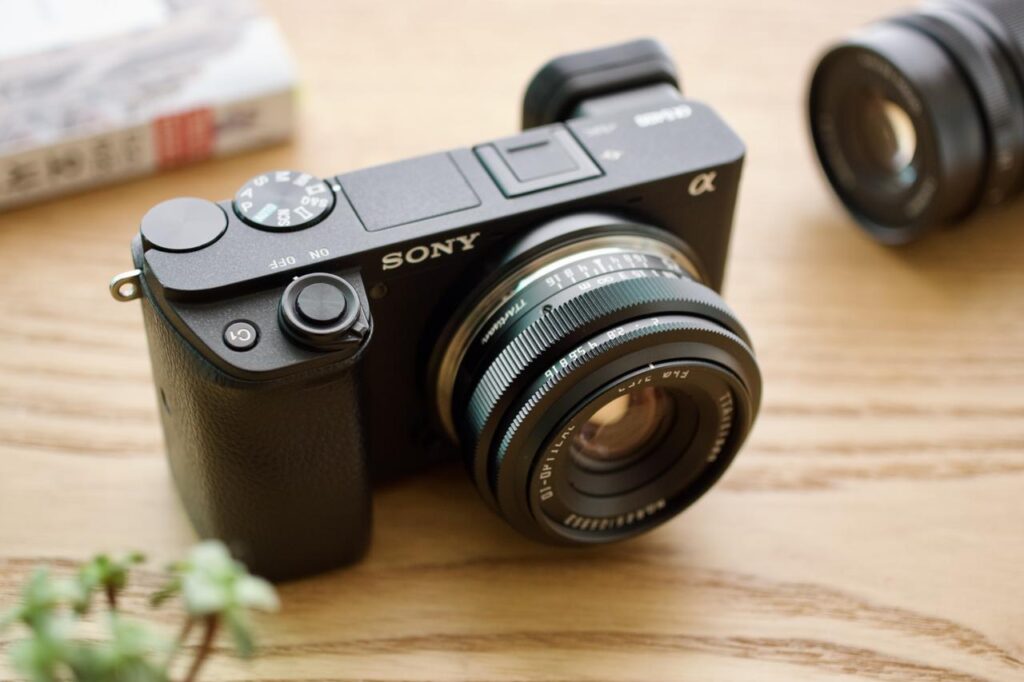 Sony A6400 mirrorless camera fitted with a TTArtisan 25mm F2 manual-focus lens on a wooden desk.