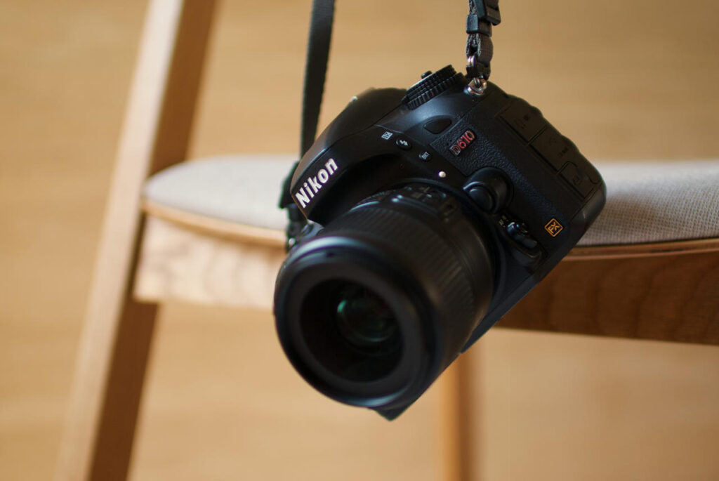 Nikon D610 DSLR with a manual-focus lens hanging from a chair by its camera strap.