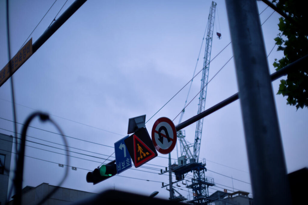 Twilight street scene photographed with a Nikon D610 and Nikkor 55mm F1.2 AI, with focus accidentally placed on a nearby sign instead of the distant construction crane.